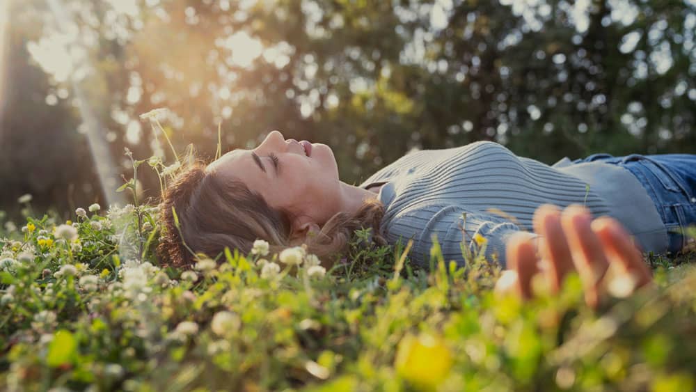 Frau liegt achtsam und entspannt im Gras unter Sonnenlicht – Symbol für Achtsamkeit und Selbstfürsorge